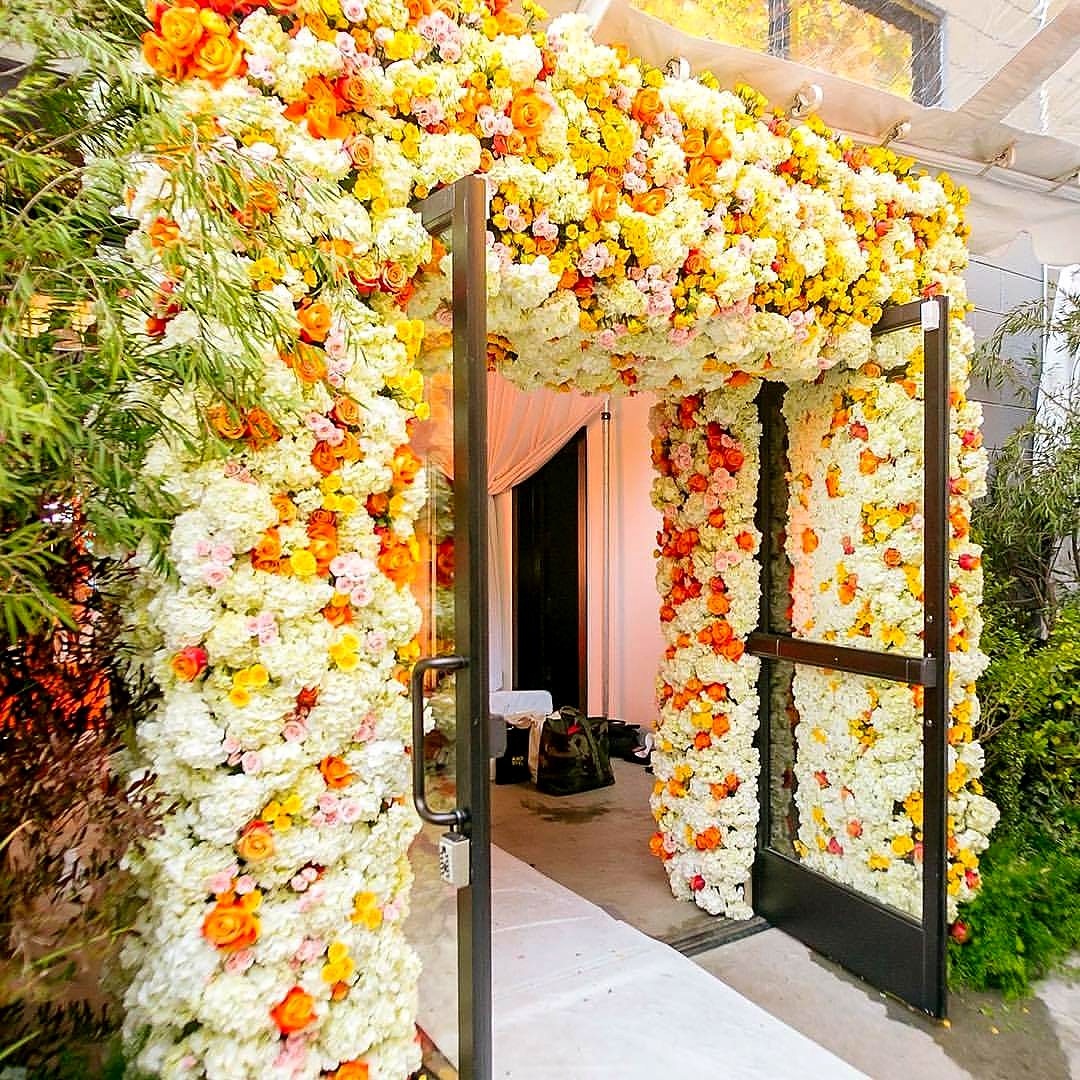 Entry arch covered in white hydrangeas with orange, yellow and pink roses