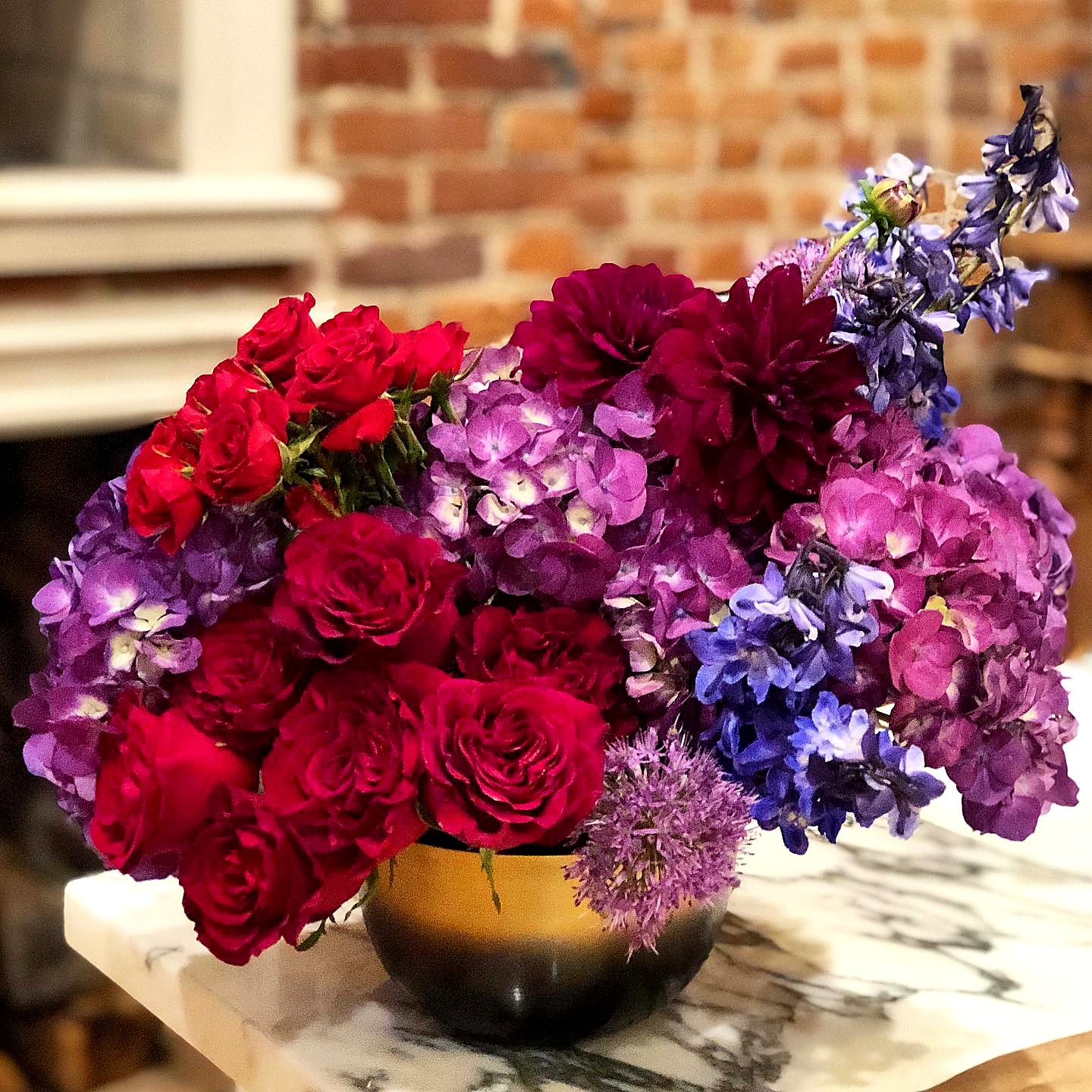 Red roses, purple hydrangea, dahlias and delphinium in a gold bowl on marble