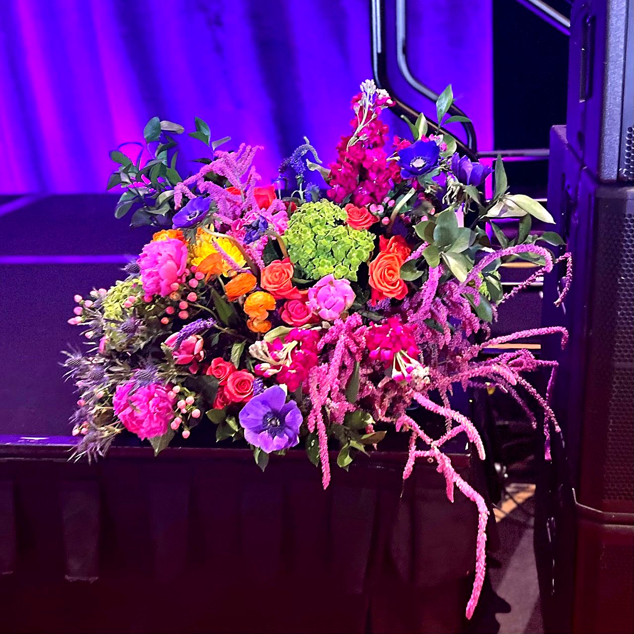 Colorful stage arrangement of peonies, roses and anemones under purple lighting