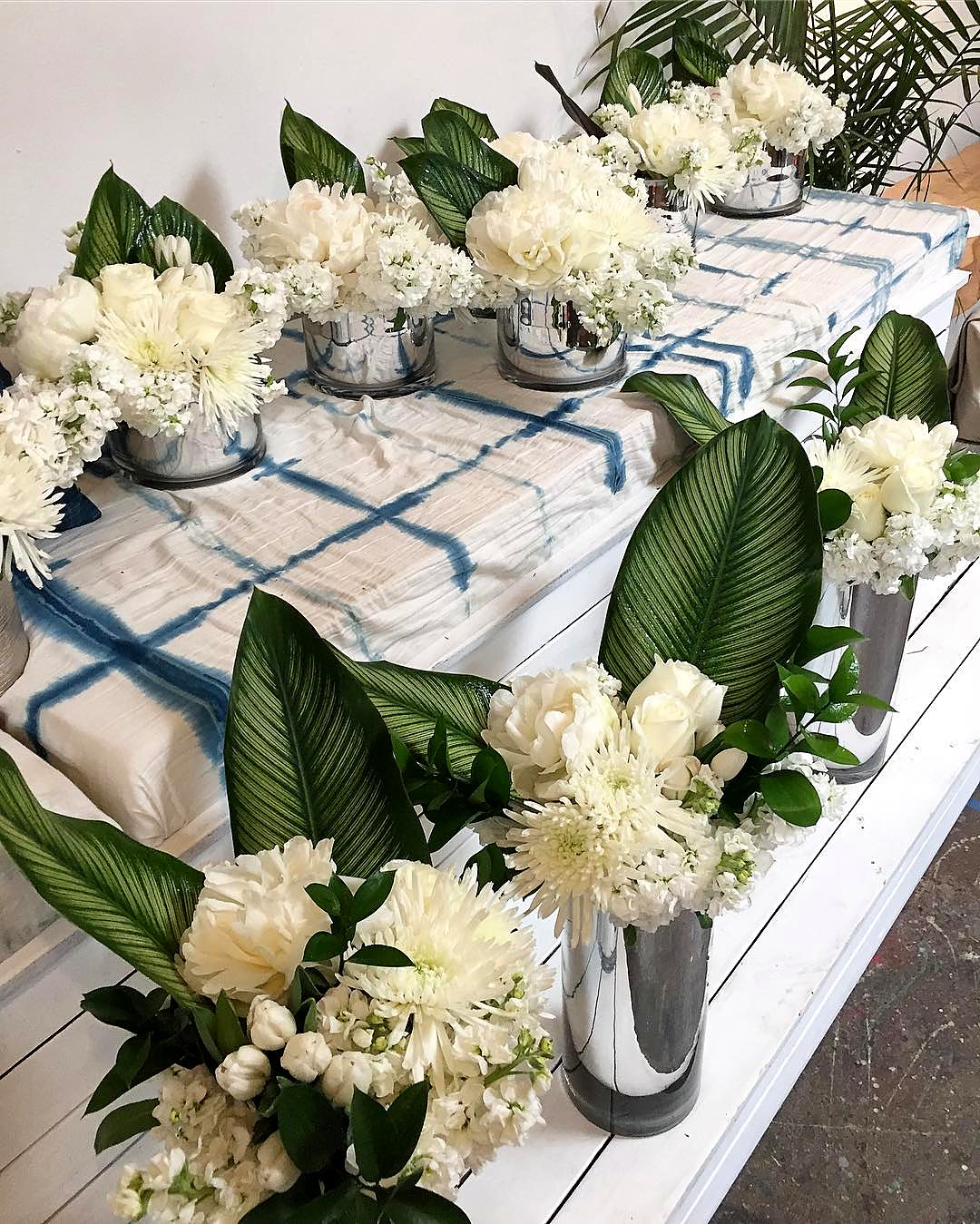 White flower arrangements with calathea leaves in mirrored silver vases on a blue shibori cloth